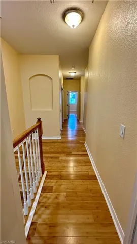 Corridor featuring an upstairs landing, a textured wall, light wood-type flooring, and a textured ceiling