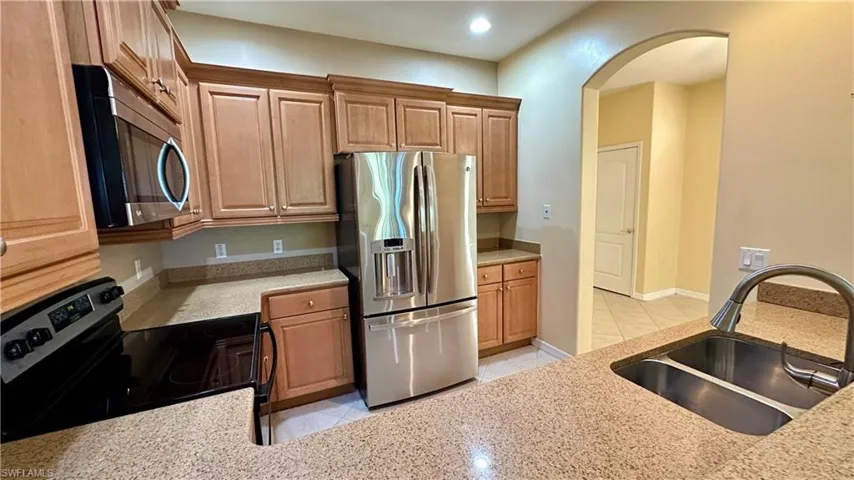 Kitchen featuring appliances with stainless steel finishes, light tile patterned floors, light stone counters, brown cabinets, and arched walkways