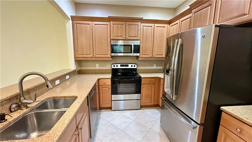 Kitchen featuring appliances with stainless steel finishes, light stone countertops, light tile patterned flooring, and brown cabinets