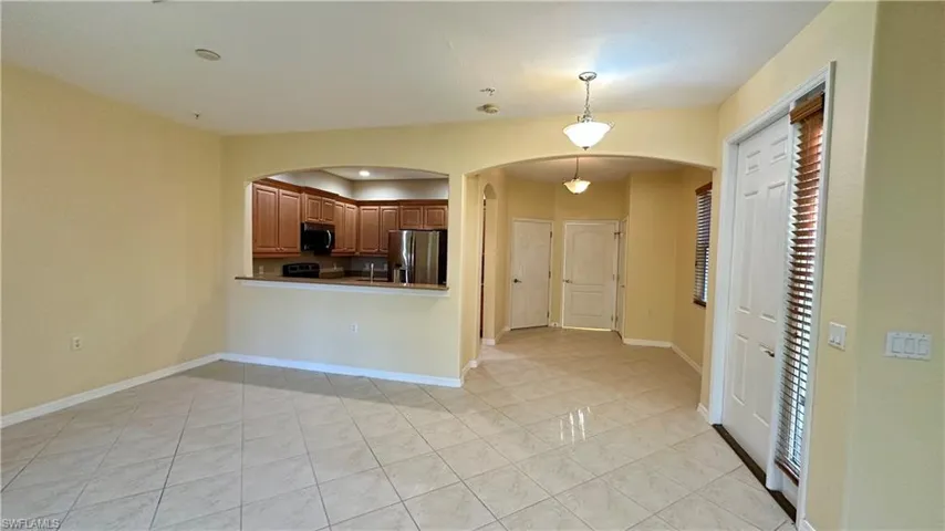 Kitchen with decorative light fixtures, arched walkways, appliances with stainless steel finishes, light tile patterned floors, and brown cabinets