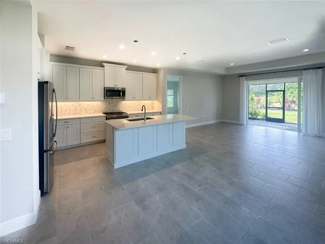 Kitchen with white cabinetry, stainless steel appliances, a center island with sink, open floor plan, and light stone countertops