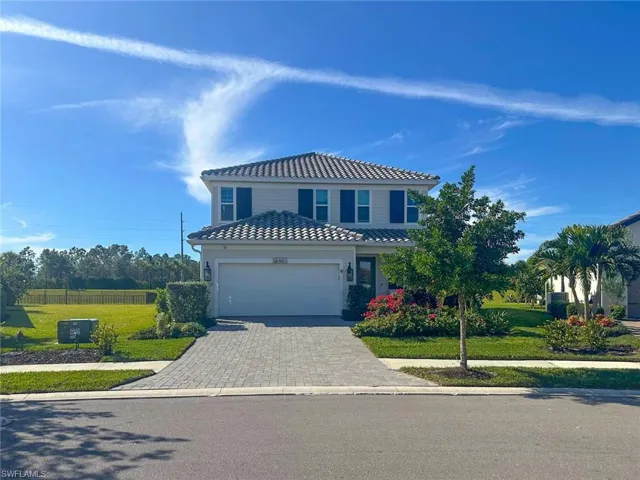 View of front of house with a tiled roof, decorative driveway, an attached garage, and a front lawn