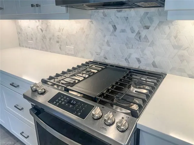 Kitchen view of decorative backsplash, stainless steel gas range oven, light stone counters, and ventilation hood