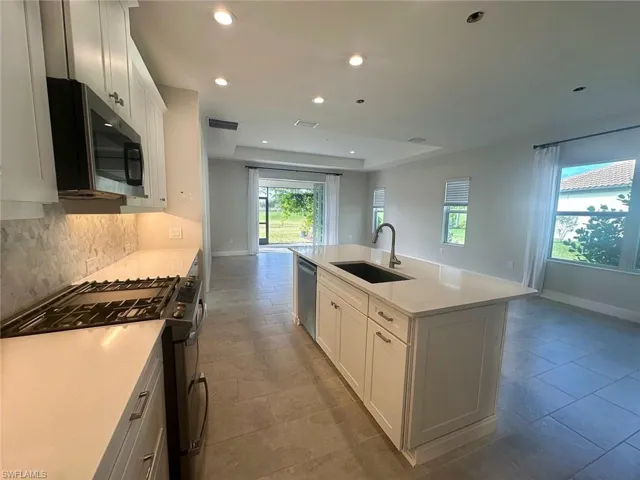 Kitchen featuring stainless steel appliances, white cabinets, a kitchen island with sink, light stone counters, and recessed lighting