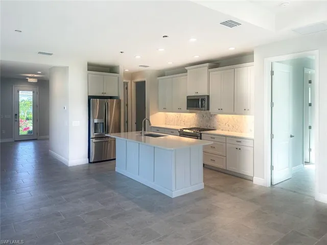 Kitchen featuring stainless steel appliances, a kitchen island with sink, tasteful backsplash, white cabinetry, and light stone countertops