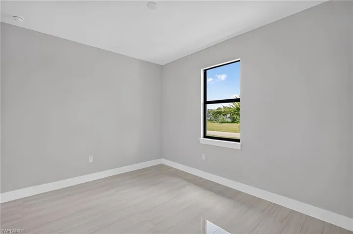 Bright interior space featuring a single window with black trim, light gray walls, white baseboards, and light wood-finish plank flooring