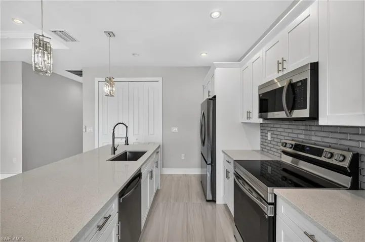Contemporary kitchen featuring an expansive island with a built-in sink, stainless steel appliances, white shaker cabinetry, a subway tile backsplash, and recessed lighting