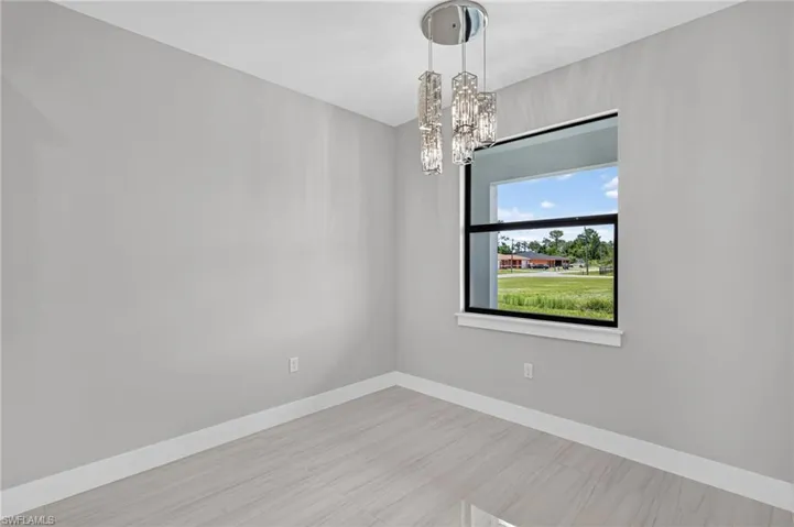 Light gray wall finishes with white trim complement the contemporary chandelier and large window framing the exterior landscape