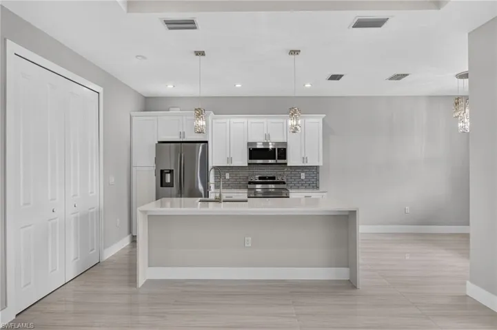 Modern kitchen featuring an island with a waterfall countertop, stainless steel appliances, white cabinetry, and a subway tile backsplash