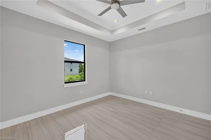 Spacious interior room featuring light wood-finish flooring, a tray ceiling with recessed lighting, and a modern ceiling fan