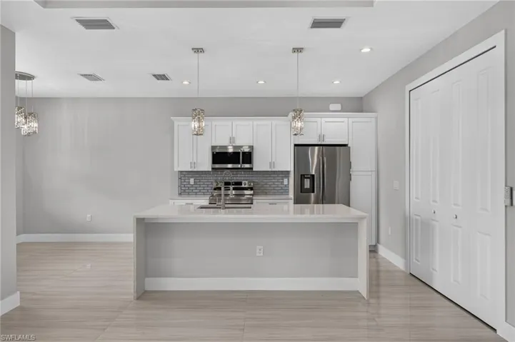 Contemporary kitchen featuring a waterfall island with a stainless steel sink, white shaker cabinetry, stainless steel appliances, and mosaic tile backsplash