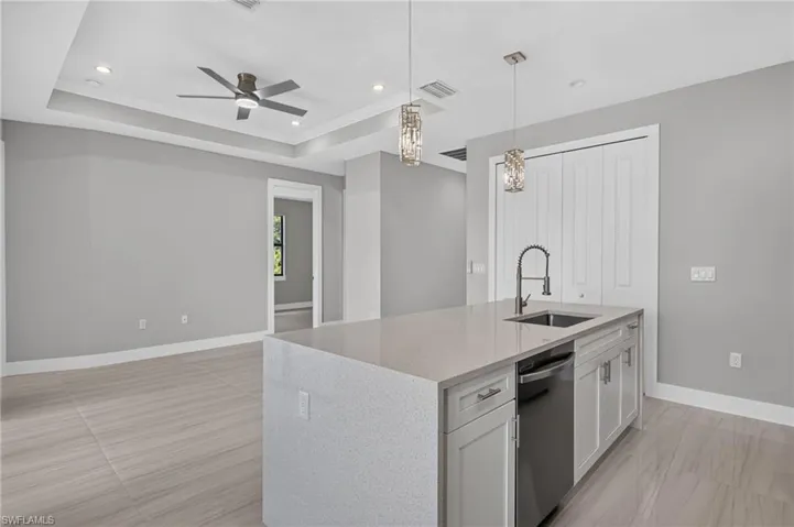 Kitchen island featuring a stainless steel sink, gooseneck faucet, dishwasher, and pendant lighting