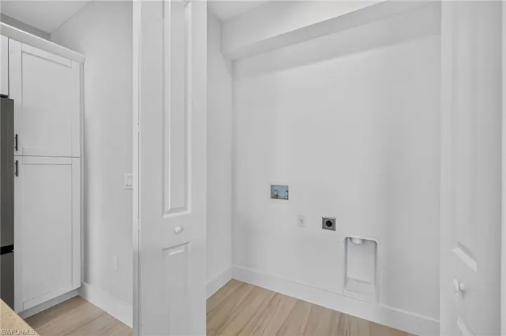 Dedicated utility area featuring connections for washer and dryer, light wood-finish flooring, and crisp white baseboards
