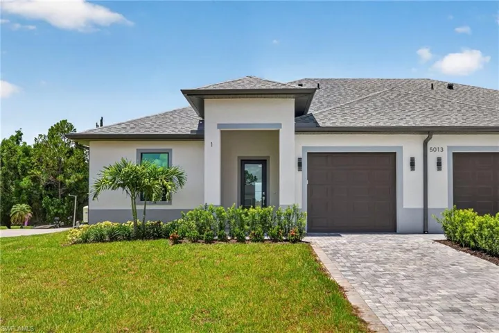 Contemporary stucco exterior with a covered entry, dark garage door, and a paver driveway