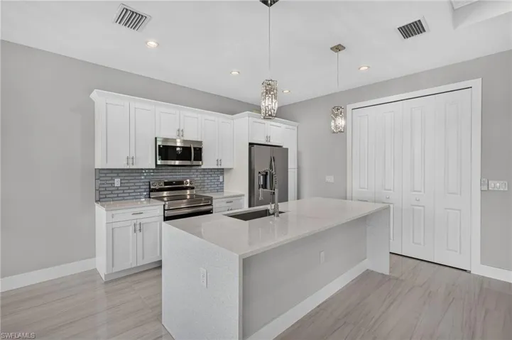 Modern kitchen featuring an island with an undermount sink, white shaker cabinetry, stainless steel appliances, a tiled backsplash, and recessed lighting