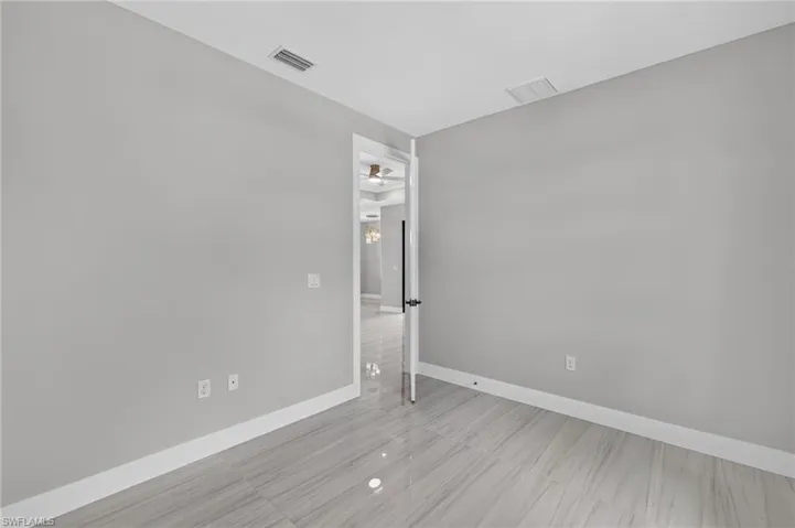 Spacious room featuring gray walls, white baseboards, and lustrous tile flooring