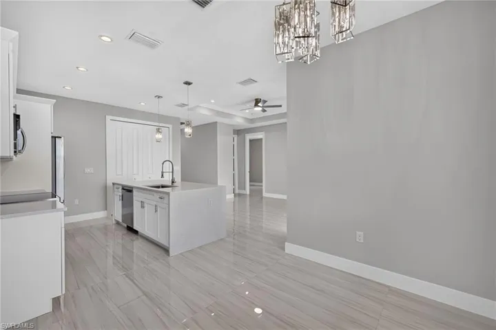 Open-concept kitchen and dining area featuring large format tile flooring, a central island with an undermount sink, white cabinetry, and stainless steel appliances