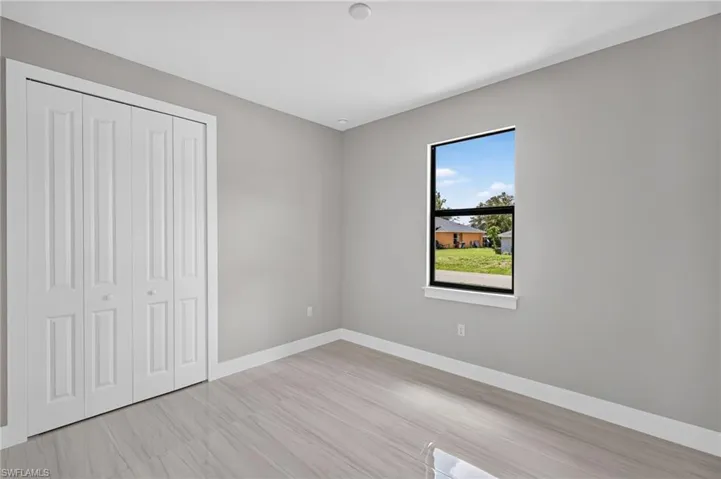 Light-filled room featuring a single-pane window with black framing, bi-fold closet doors, recessed ceiling lighting, light grey walls, and wood-finish flooring