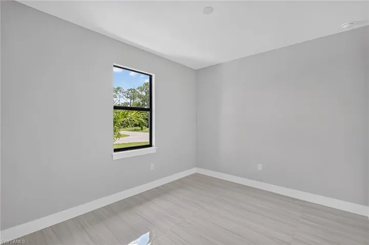 Spacious room featuring light gray walls, large format tile flooring, and a window with black trim