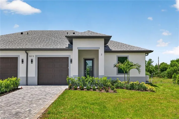 Modern stucco exterior featuring a covered entry, decorative garage doors, and a paver driveway