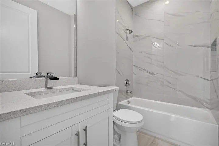 Contemporary bathroom featuring a white vanity with a light speckled countertop, chrome waterfall faucet, and a built-in rectangular sink