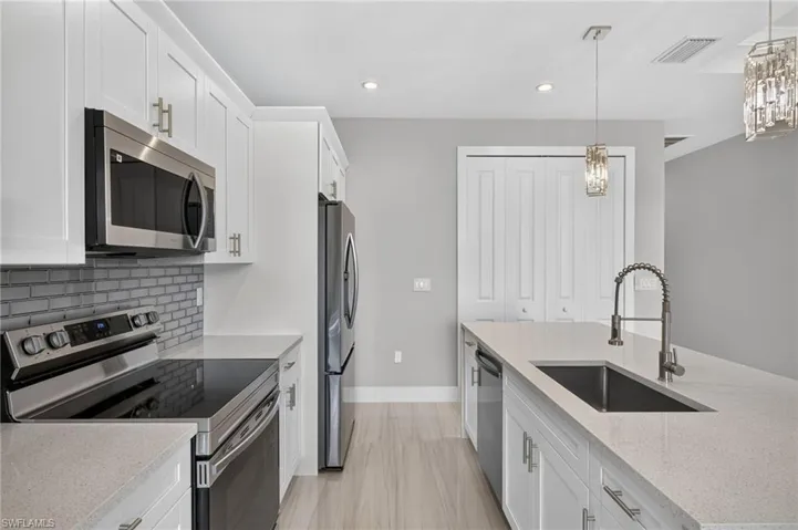 Modern kitchen featuring an island with an undermount sink and pull-down faucet, white shaker cabinetry with brushed nickel hardware, light-toned countertops, and stainless steel appliances