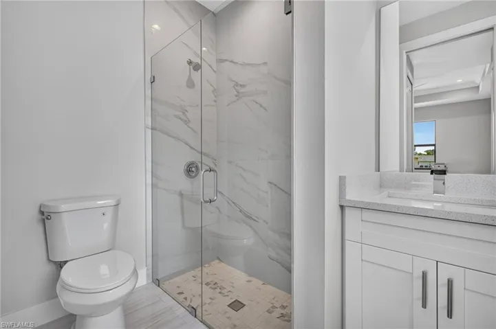 Bathroom featuring a frameless glass shower enclosure, large format marble-look tile shower walls, a white vanity with a quartz countertop, and a rectangular undermount sink with a chrome faucet