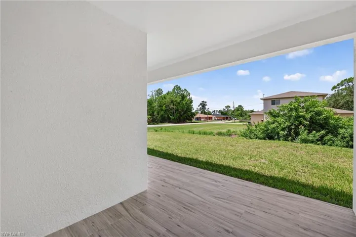 Covered outdoor area featuring wood-finish flooring, textured white walls, and an expansive grassy yard