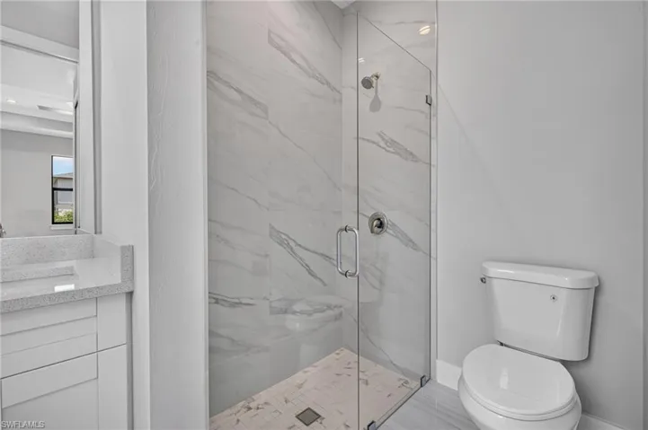 Walk-in shower with clear glass enclosure, large format white tile walls with grey veining, and a tiled shower pan