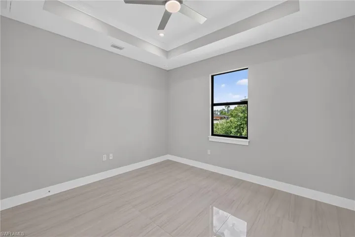 Spacious room featuring light gray walls, large format tile flooring, and a tray ceiling with a modern ceiling fan