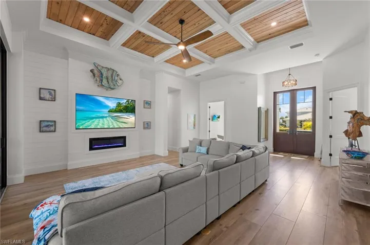 Living room with a high wood beamed ceiling, coffered ceiling, a ceiling fan, french doors, and light wood finished floors