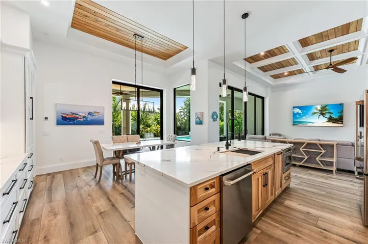 Kitchen with wood ceiling, decorative light fixtures, light wood-type flooring, light stone counters, and stainless steel appliances