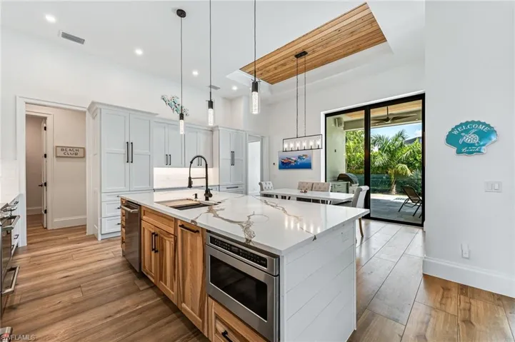 Kitchen featuring brown cabinetry, light stone countertops, pendant lighting, a raised ceiling, and light wood-style flooring