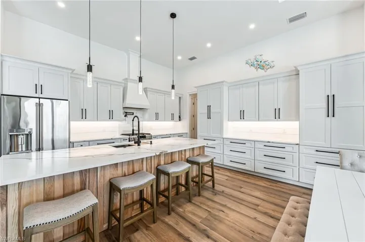 Kitchen featuring decorative light fixtures, high end fridge, light stone countertops, white cabinets, and recessed lighting