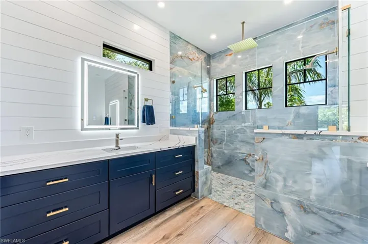 Full bathroom featuring plenty of natural light, vanity, a marble finish shower, wooden walls, and recessed lighting