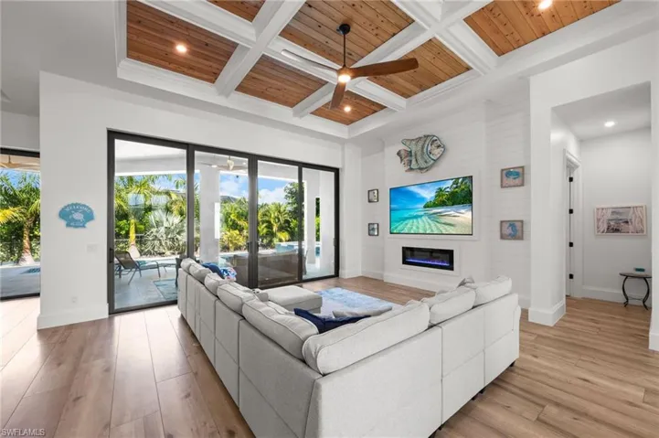 Living room featuring coffered ceiling, ceiling fan, a high wooden beamed ceiling, recessed lighting, and a glass covered fireplace