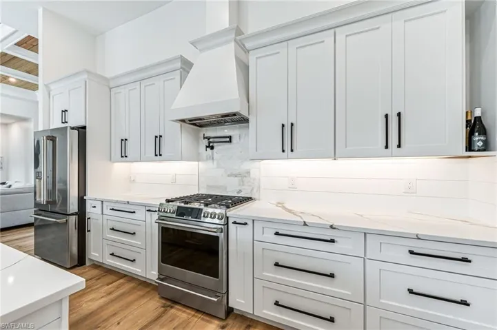 Kitchen with stainless steel appliances, light stone counters, white cabinets, light wood finished floors, and premium range hood