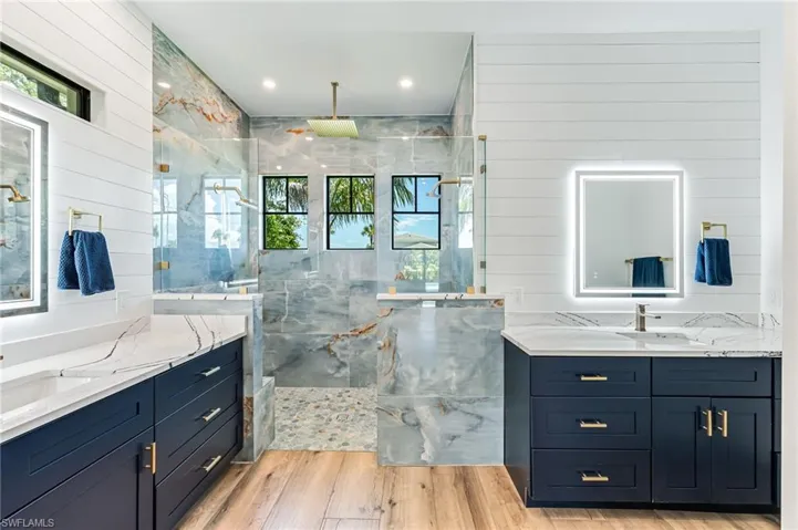 Full bathroom with two vanities, a marble finish shower, wooden walls, light wood-style floors, and recessed lighting