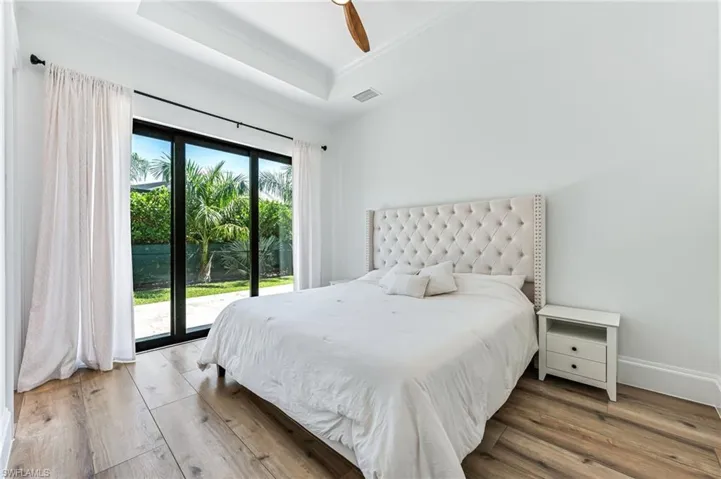 Bedroom featuring access to outside, wood-type flooring, a raised ceiling, and a ceiling fan