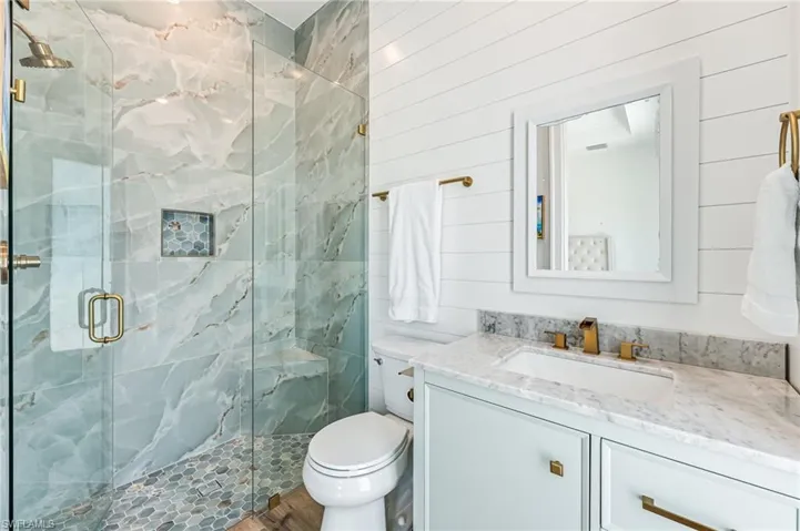 Full bath with a marble finish shower, vanity, and wooden walls