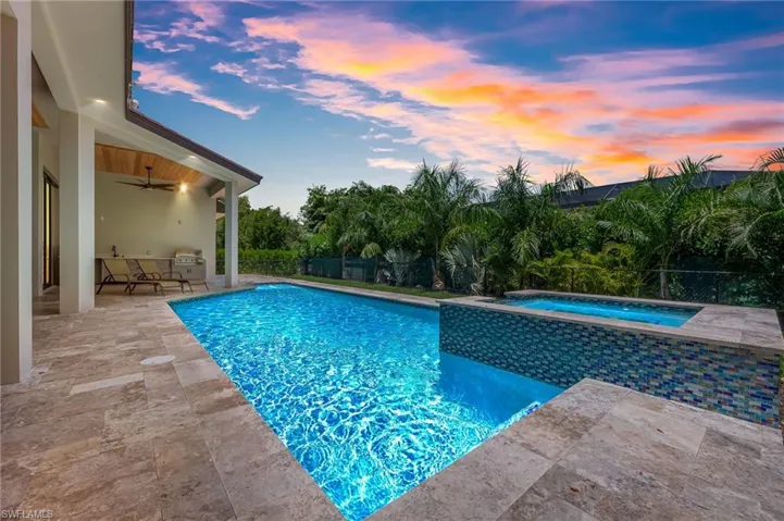 Pool at dusk featuring a patio area, a fenced backyard, and a pool with connected hot tub
