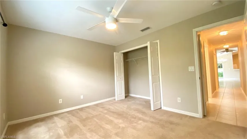 Unfurnished bedroom featuring light carpet, a closet, a ceiling fan, and light tile patterned floors