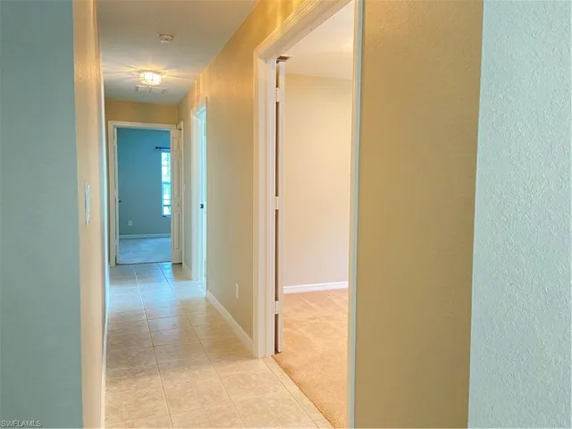 Hall with light tile patterned flooring, light carpet, and a textured wall