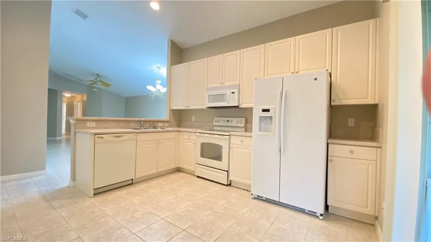 Kitchen with white appliances, light countertops, a chandelier, white cabinetry, and ceiling fan