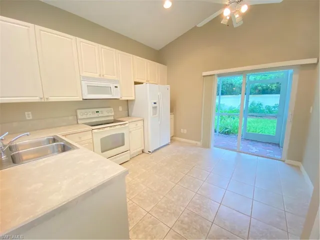 Kitchen with stove, light countertops, light tile patterned flooring, white cabinetry, and white refrigerator with ice dispenser