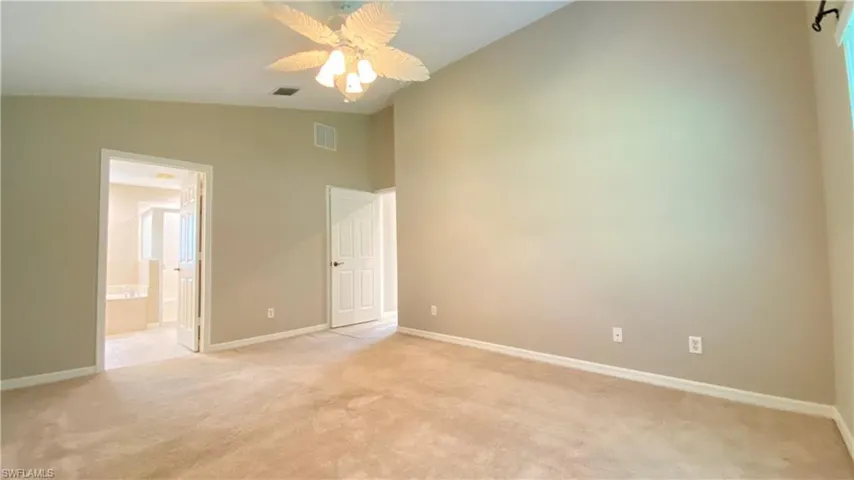 Unfurnished bedroom with light colored carpet, ensuite bath, high vaulted ceiling, and ceiling fan