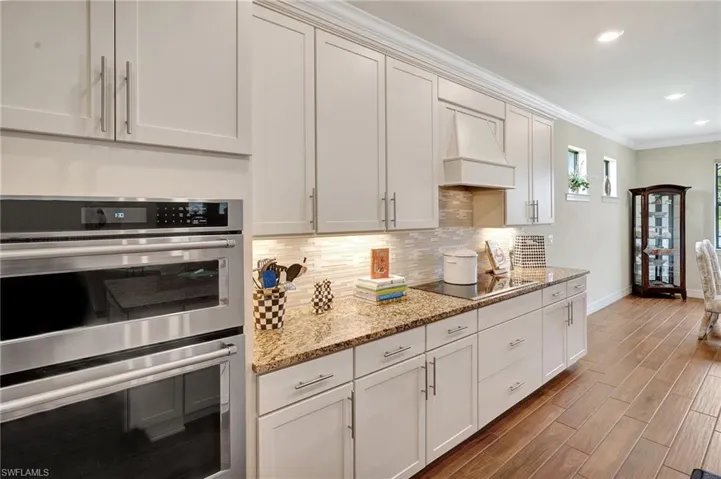 Kitchen featuring stainless steel double oven, light stone countertops, ornamental molding, decorative backsplash, and premium range hood