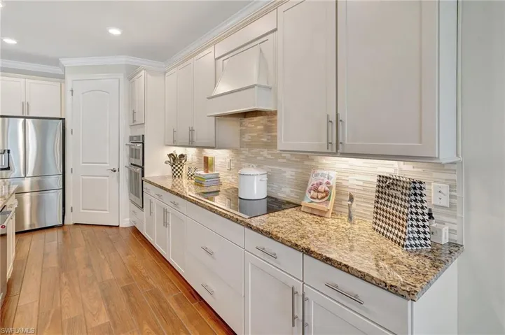 Kitchen with appliances with stainless steel finishes, backsplash, premium range hood, light stone countertops, and light wood-type flooring