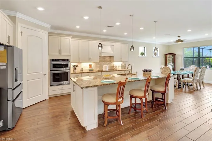 Kitchen featuring hanging light fixtures, appliances with stainless steel finishes, light stone counters, crown molding, and a kitchen bar