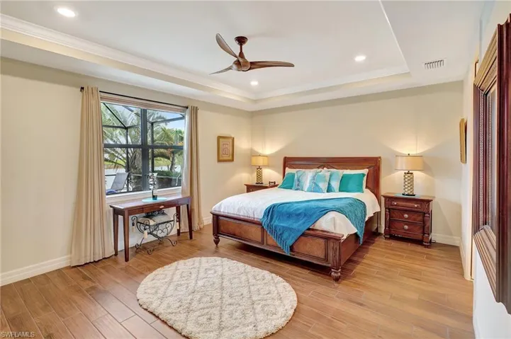 Bedroom with recessed lighting, a ceiling fan, light wood-style floors, a raised ceiling, and ornamental molding